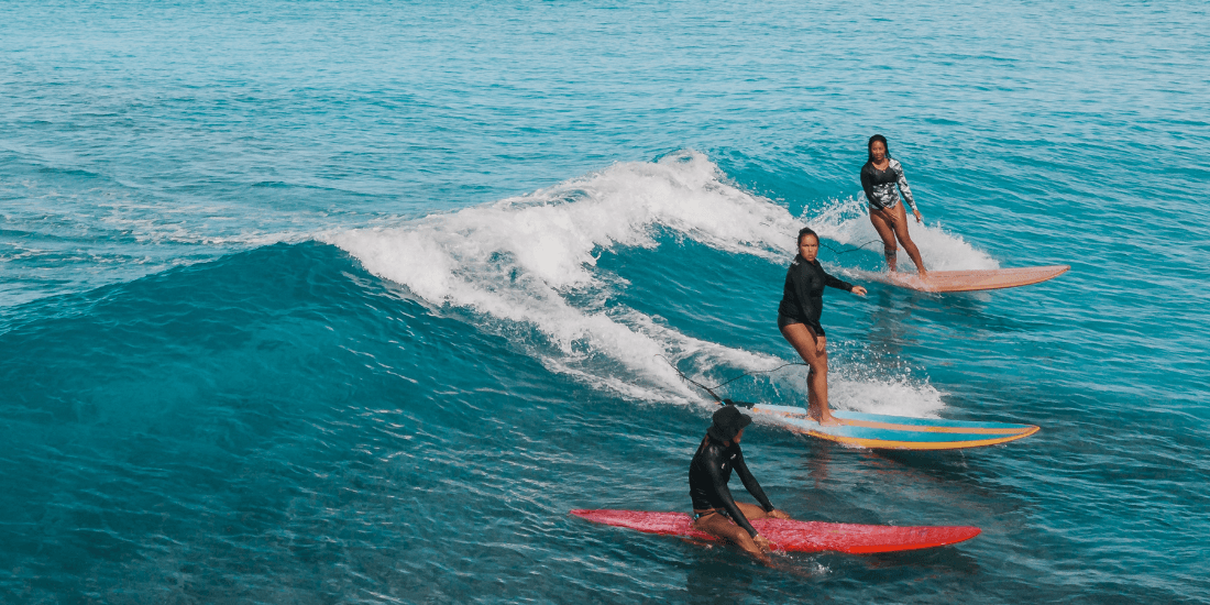 Surfers riding a small wave in clear turquoise water.