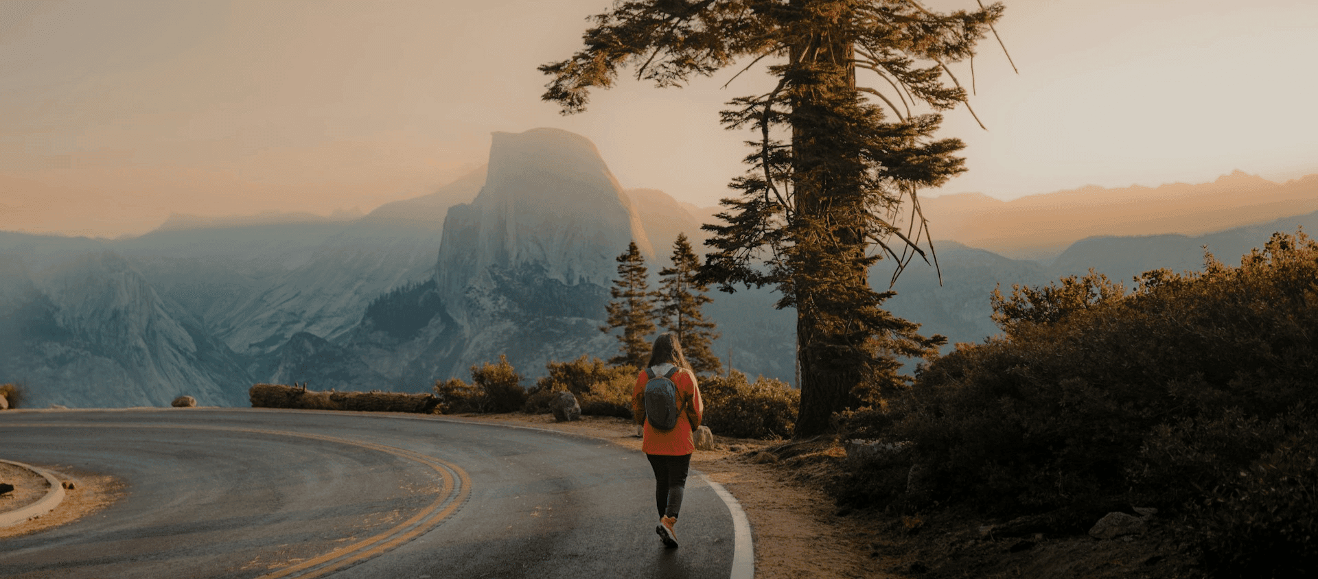Hiker walking a mountain road with Half Dome in Yosemite at sunset.