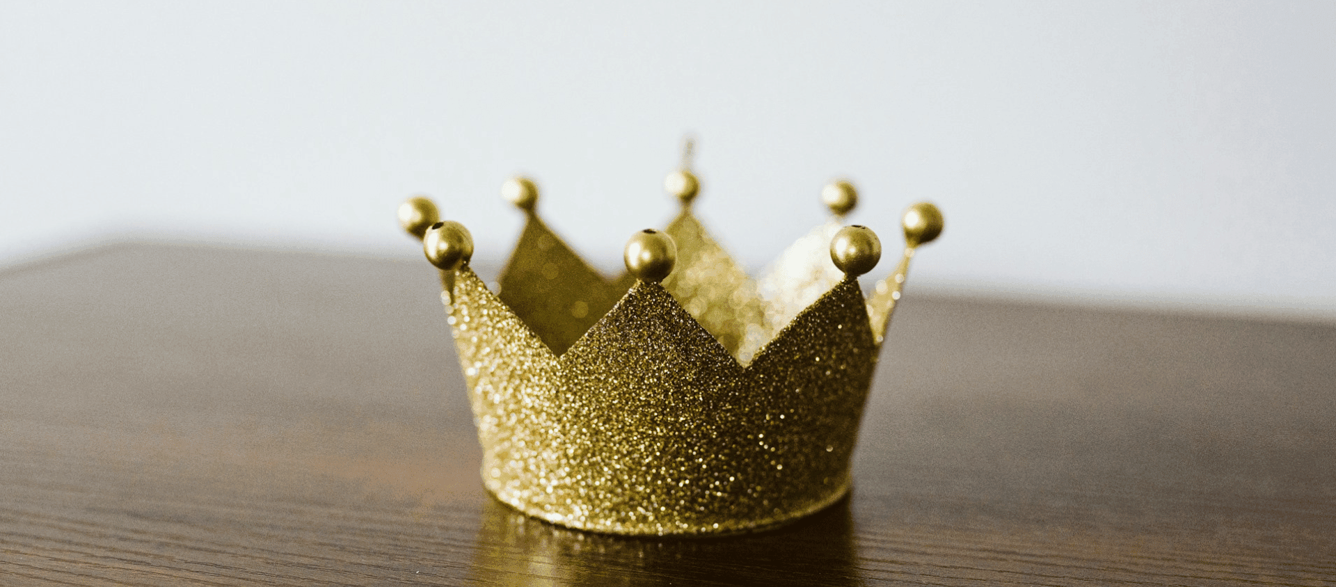 A small glittery gold crown resting on a wooden surface.