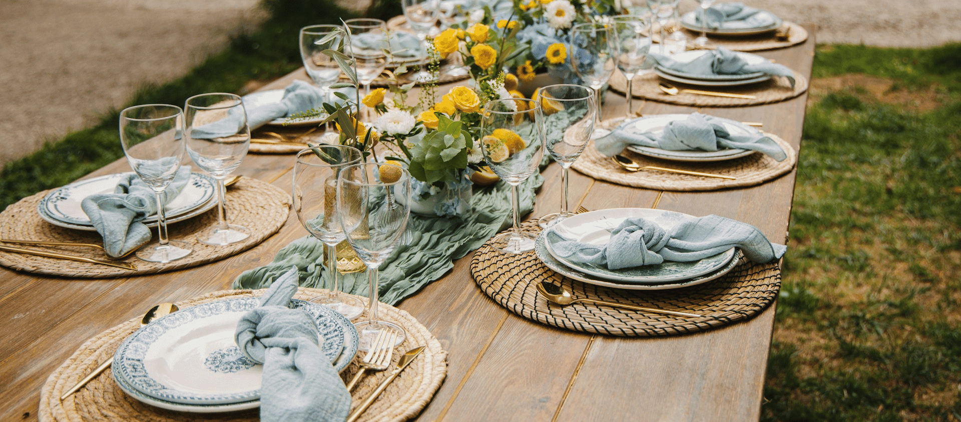 Outdoor dining table set with plates, glassware, and floral centerpiece.