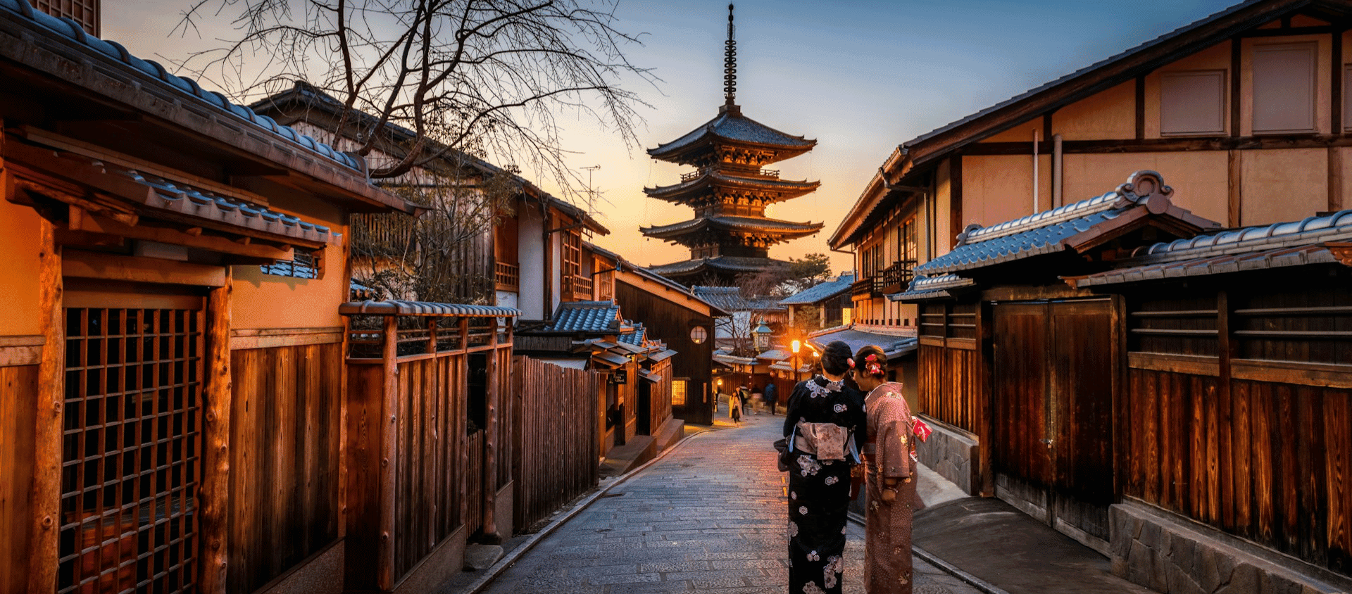 Traditional wooden street in Kyoto with pagoda at sunset.