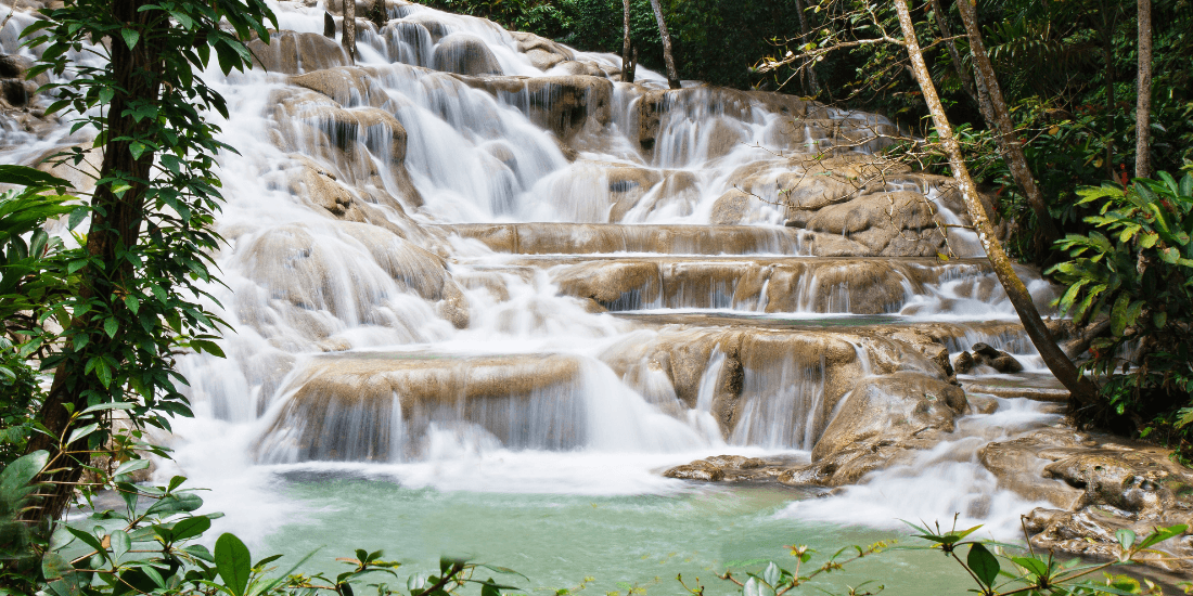 Tiered waterfall cascading over smooth rocks in a lush tropical forest.