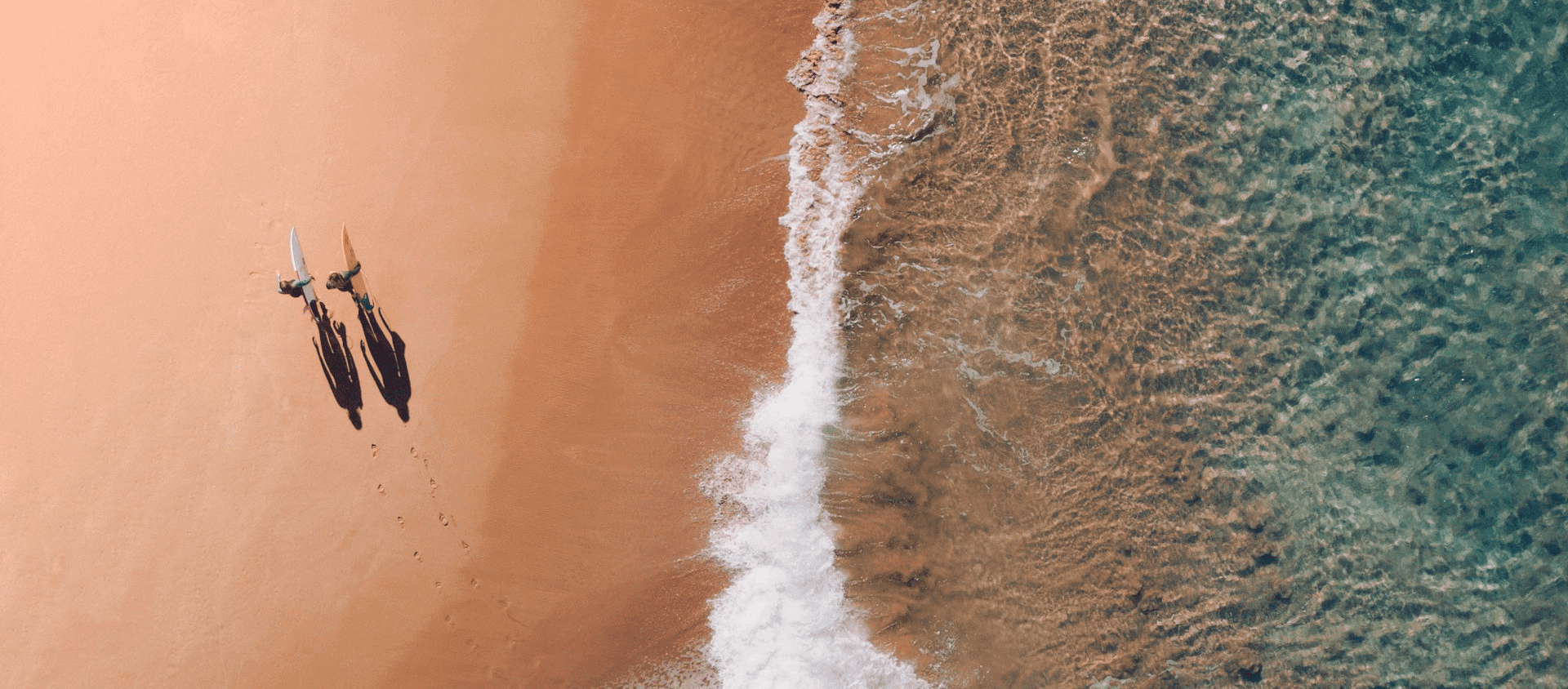 Aerial view of two people walking along an Australian beach where blue water meets golden sand.