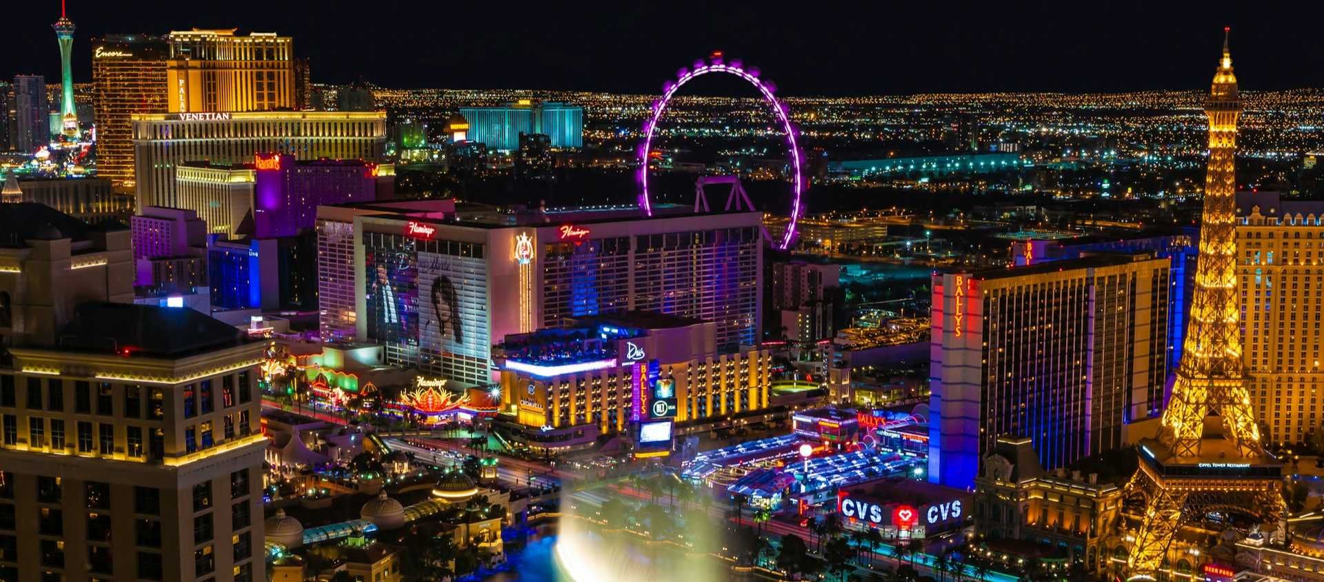 The Las Vegas Strip lit up at night with the Bellagio fountains and High Roller wheel.