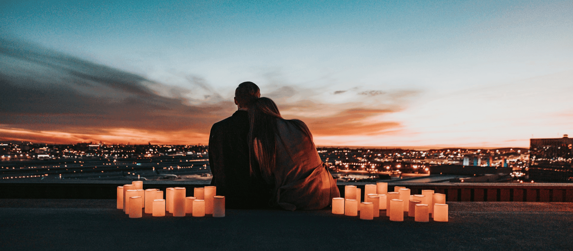 A couple sitting on the field facing the beautiful city.