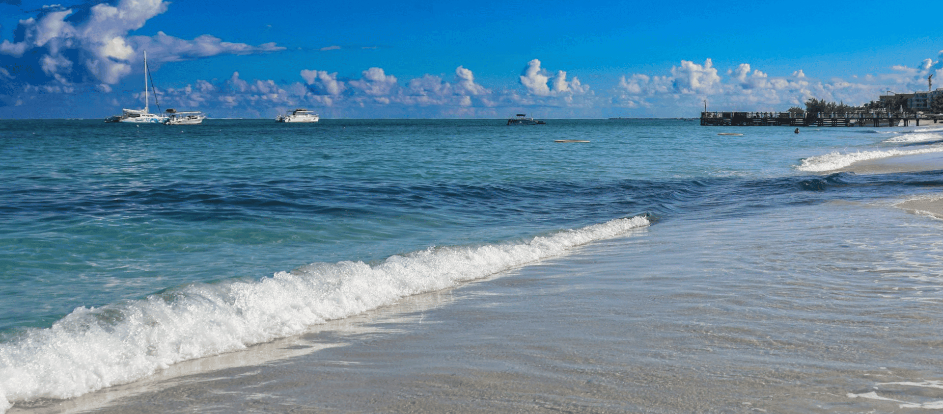 Sailboats anchored off a calm white-sand shoreline in Turks and Caicos.