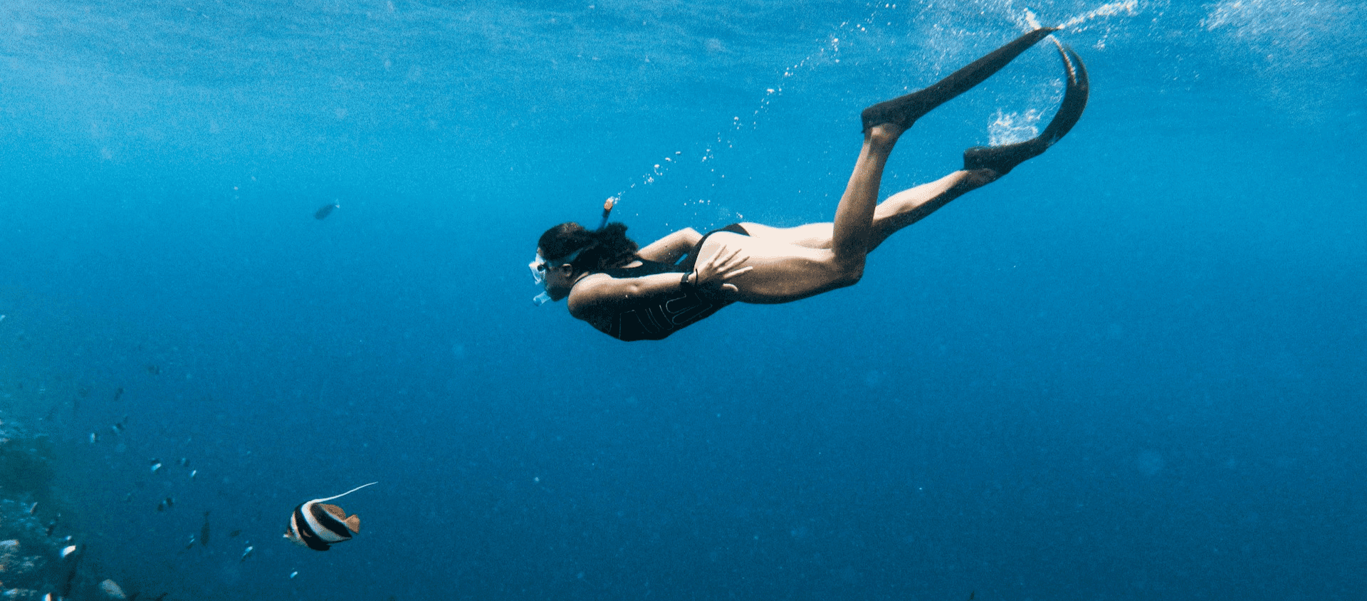 Snorkeler swimming through deep blue tropical water with fins and colorful reef fish.