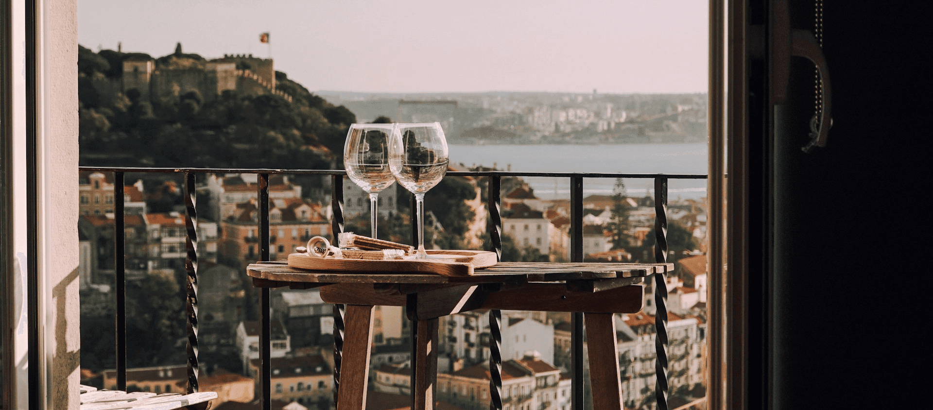 Wine glasses on a rooftop table overlooking the Lisbon cityscape and hilltop castle.