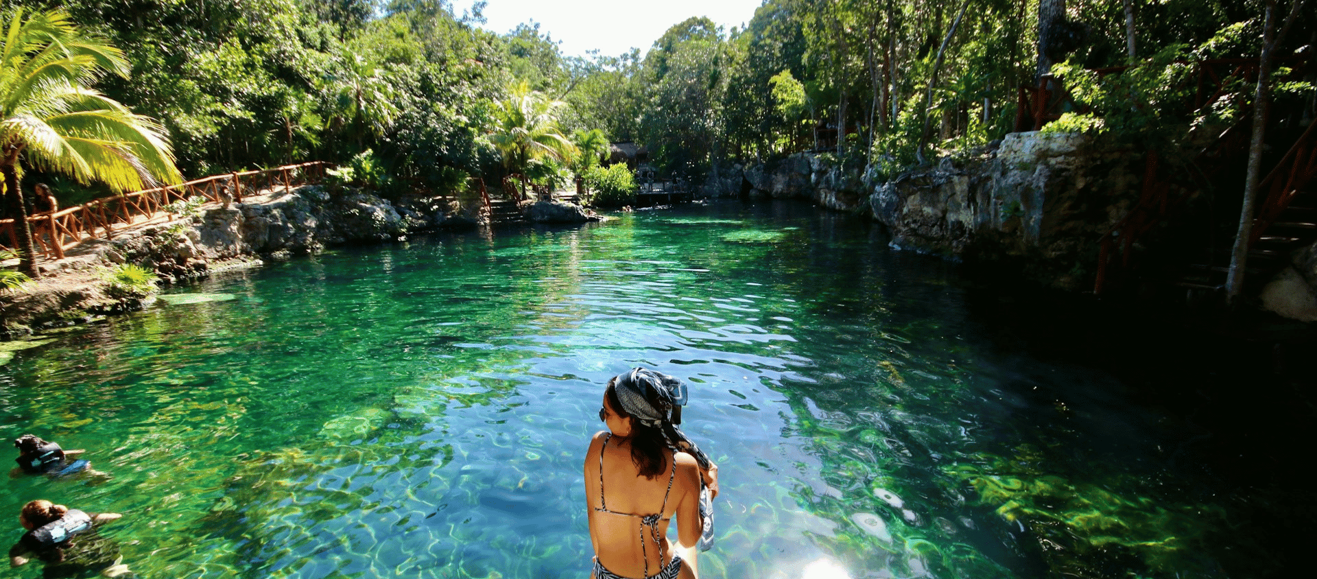 Woman wading in the crystal clear turquoise water of a jungle cenote in Tulum.