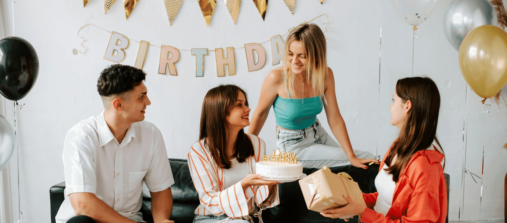 Group of friends celebrating a birthday together with cake and balloons.