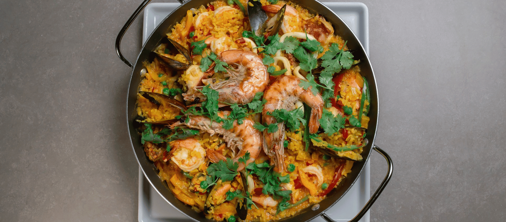 Seafood paella in a large pan with shrimp and herbs.