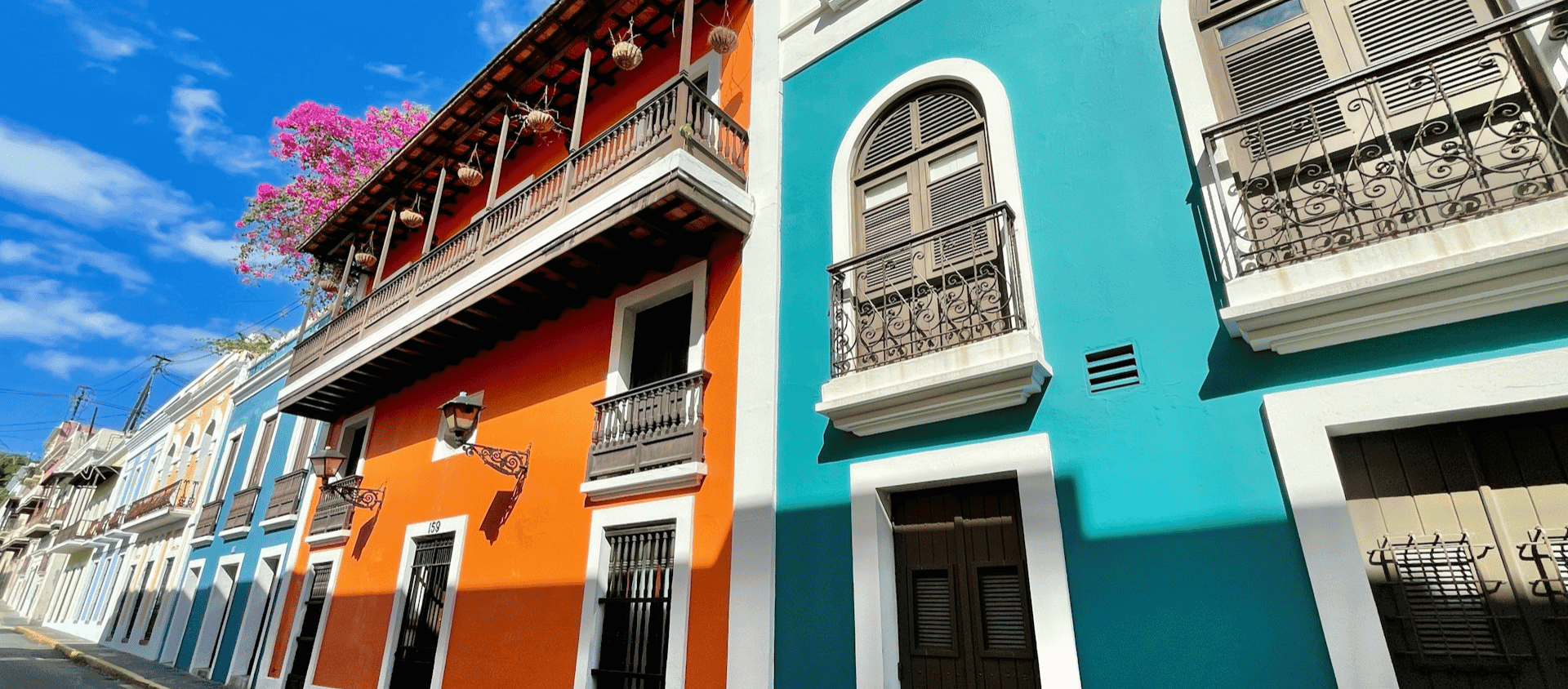 Brightly painted historic buildings with wrought iron balconies under a clear blue sky.