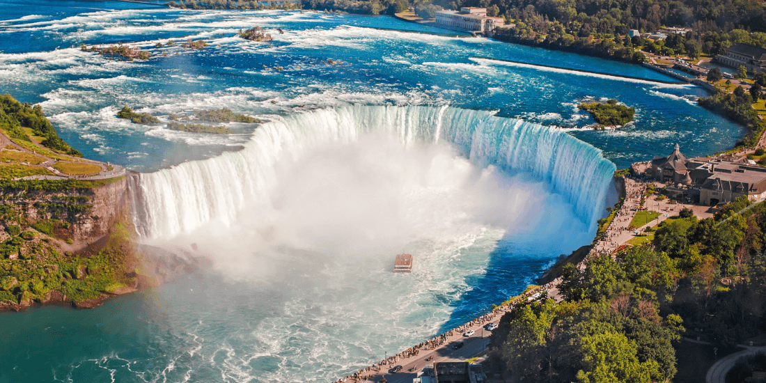 Aerial view of a large waterfall with mist rising and a tour boat below.