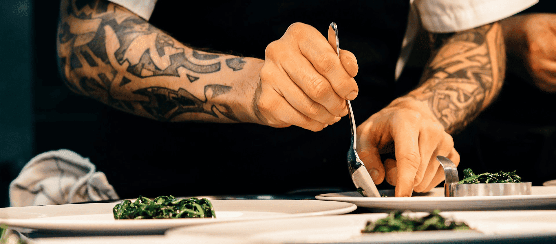 A chef plating food carefully with tweezers in a professional kitchen.