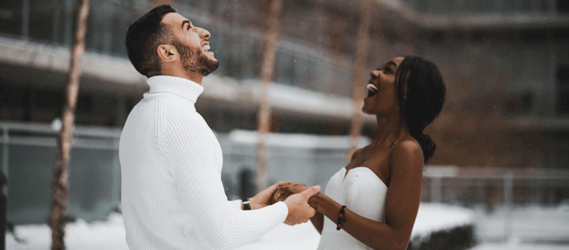 Laughing couple holding hands in a snowy outdoor setting.