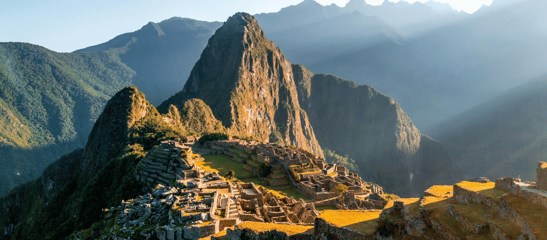 Sunrise over the Machu Picchu citadel and surrounding green mountain peaks.