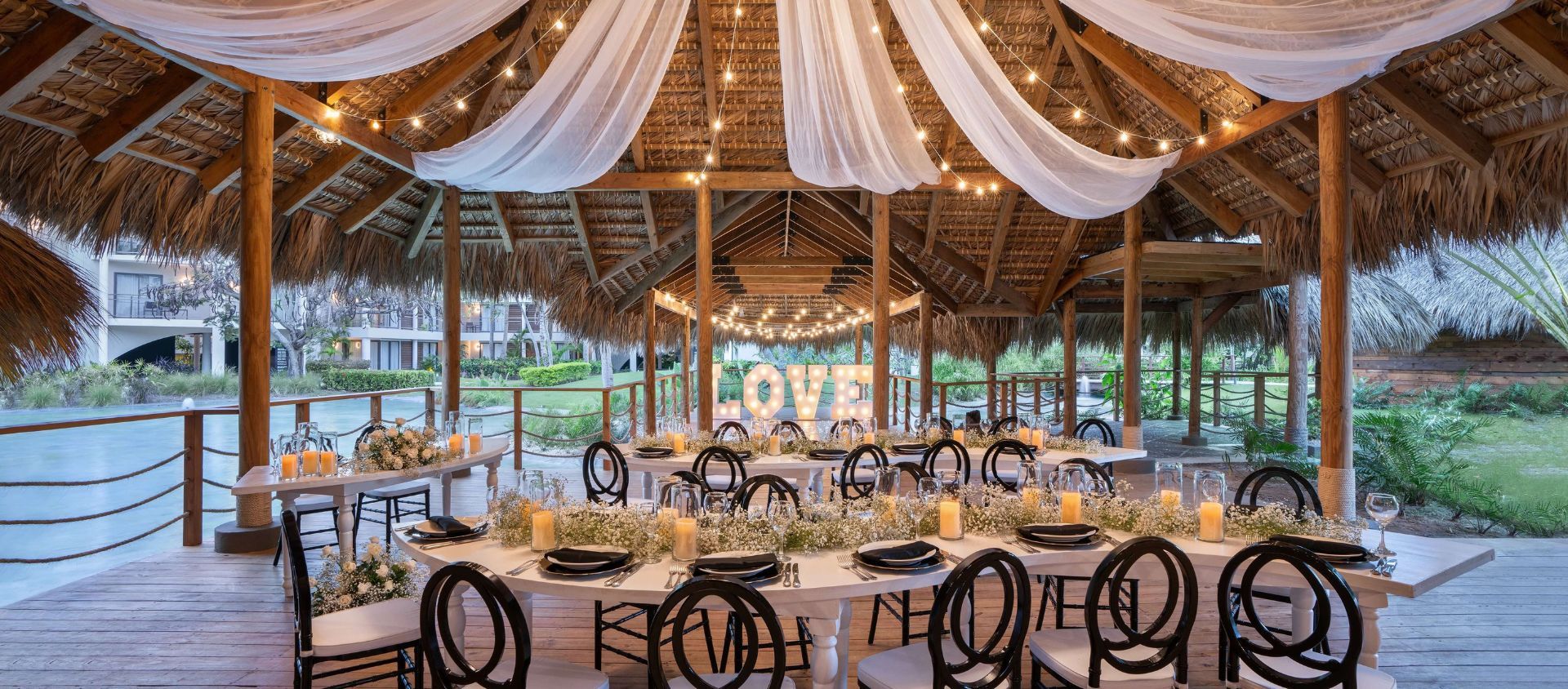 Wedding reception with draped fabric, string lights, and a glowing love sign.