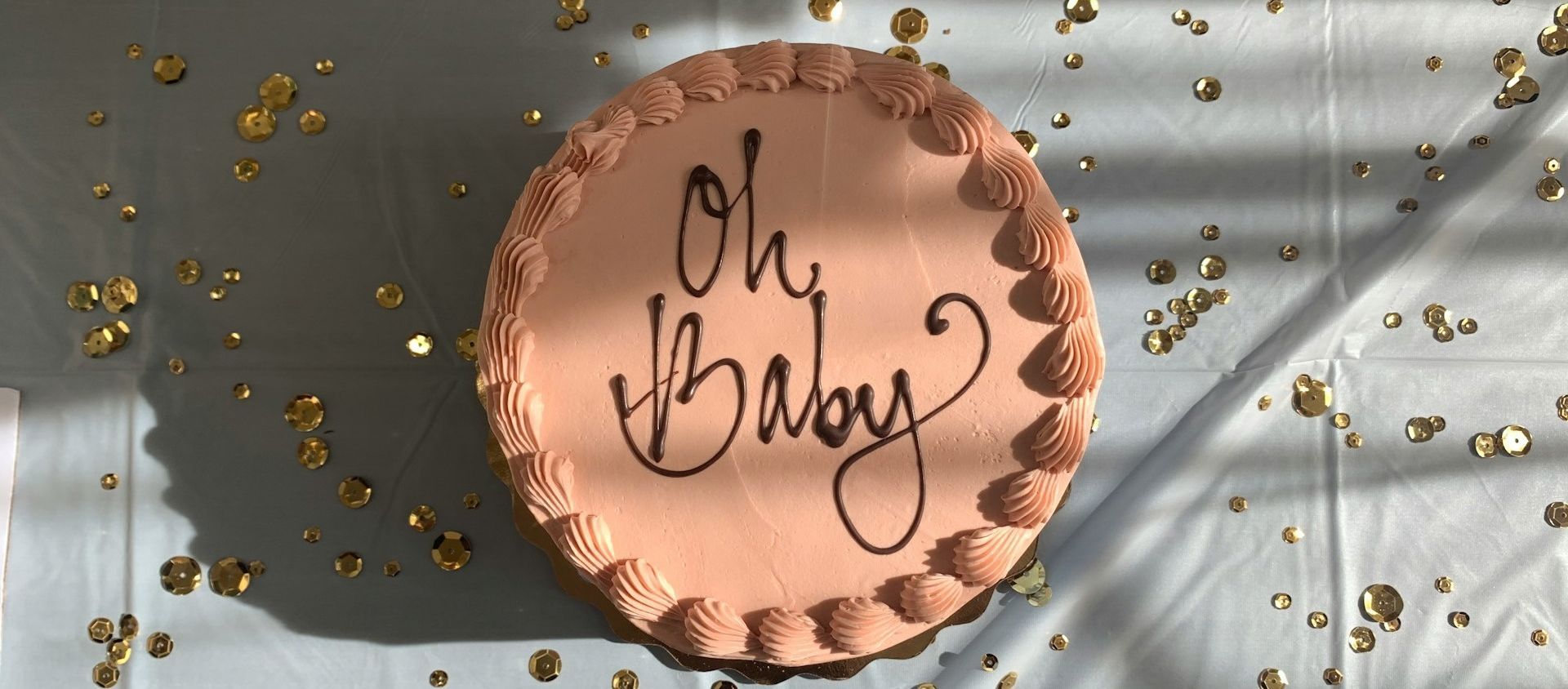 A pink 'Oh Baby' cake surrounded by gold confetti.