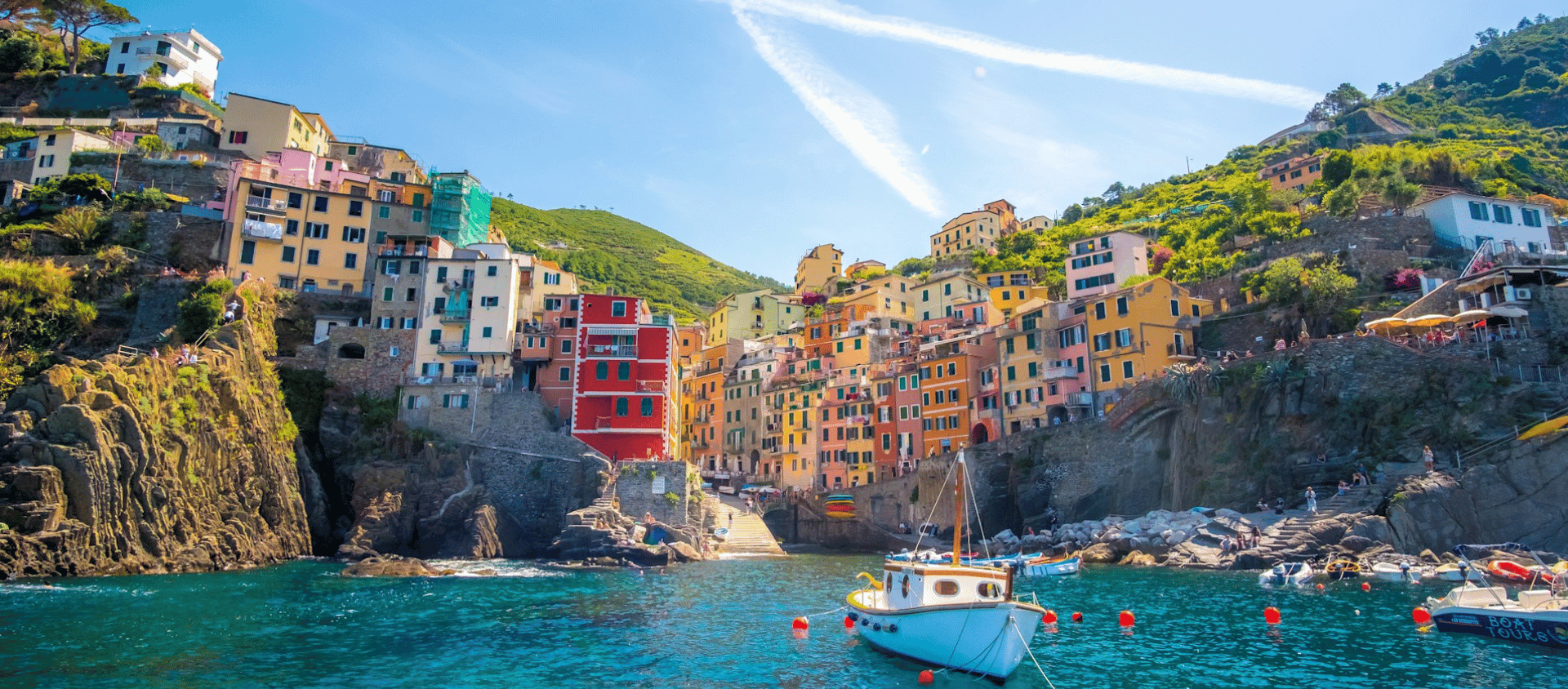 Colorful cliffside homes overlooking a bright blue harbor with boats in Cinque Terre.