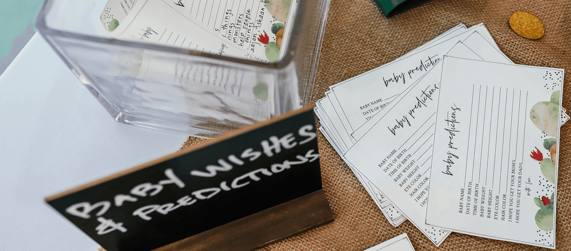 Baby prediction cards and a sign on a table at a baby shower activity station.