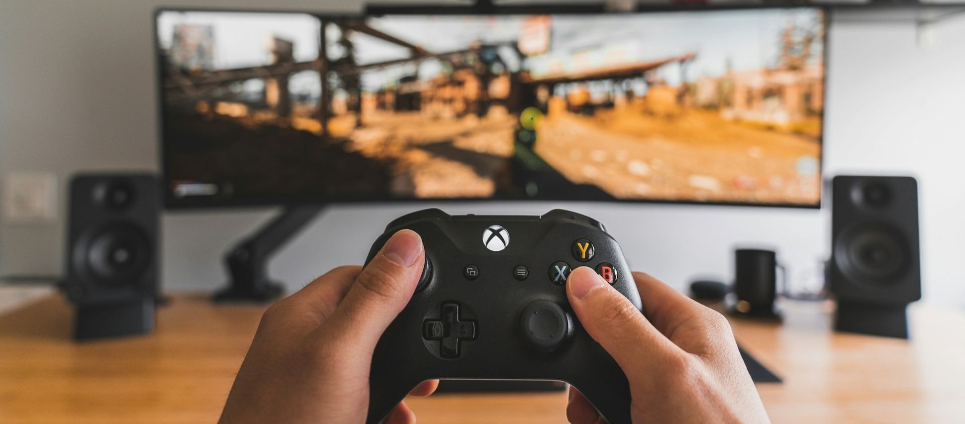 Hands holding an Xbox controller in front of a gaming monitor.