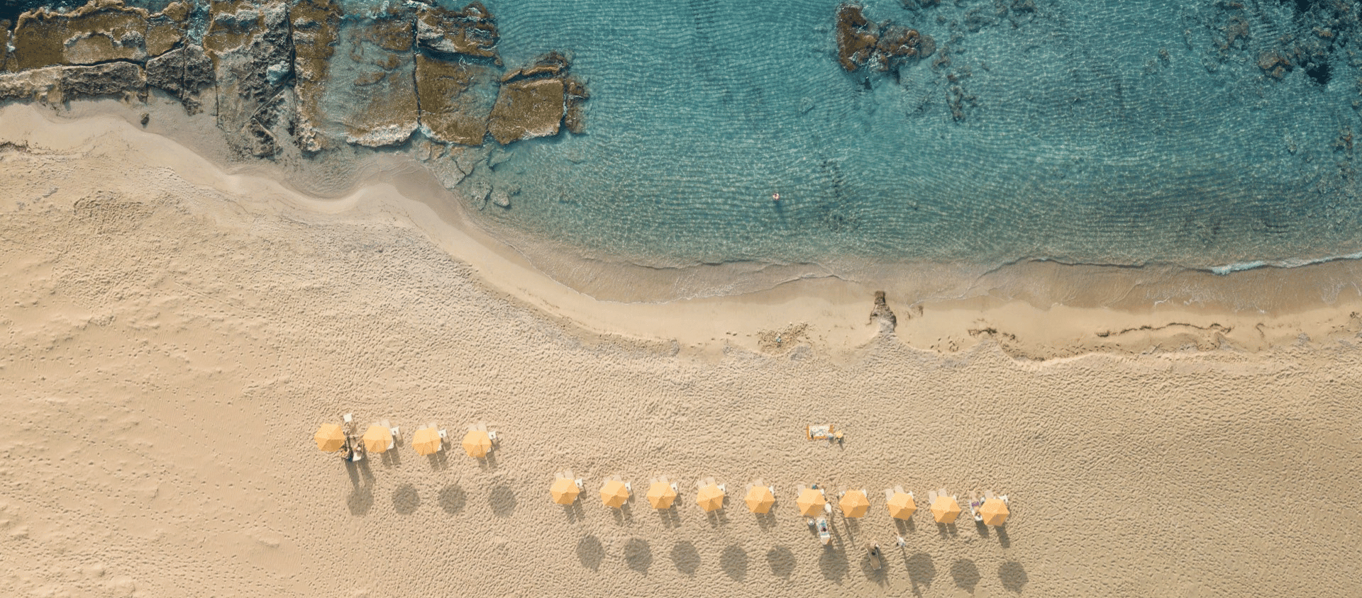 Aerial view of sandy beach with umbrellas and clear blue shoreline