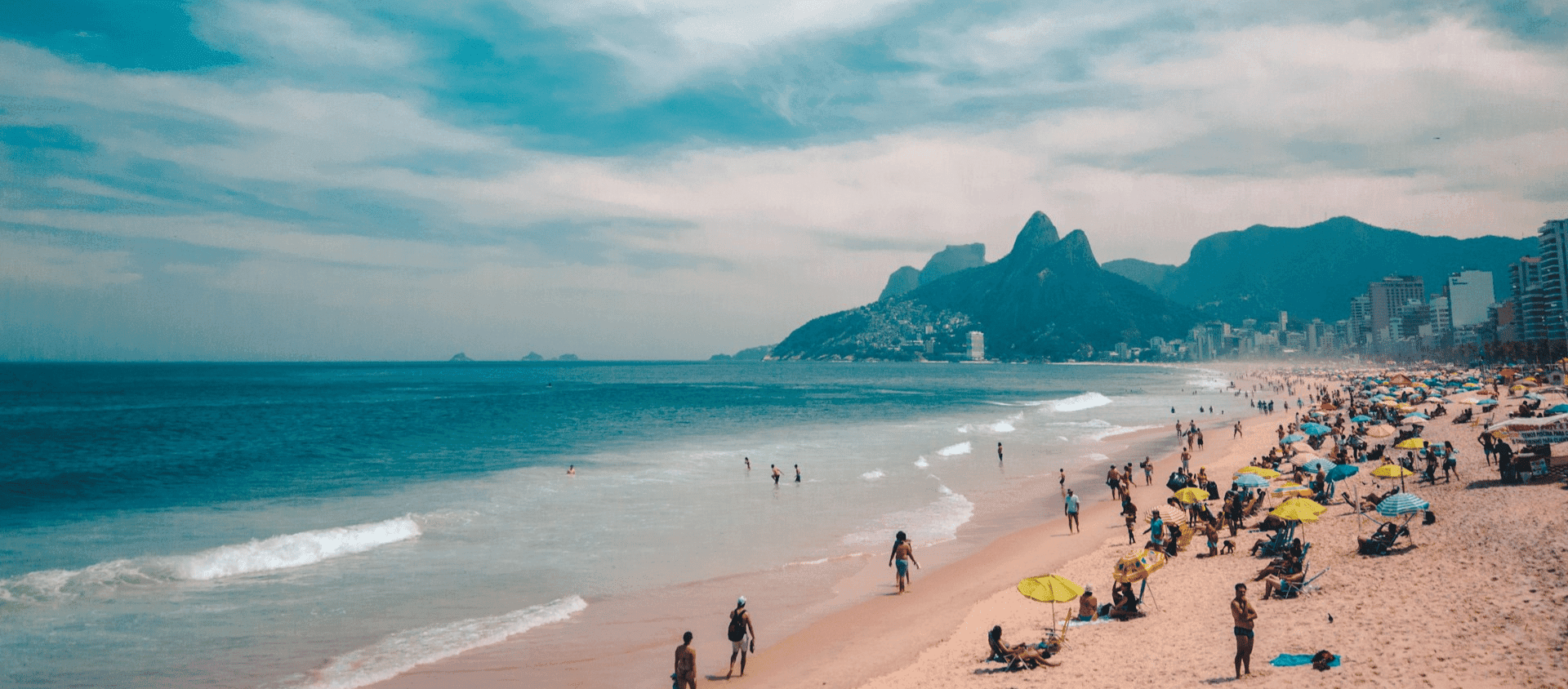 Crowds and umbrellas on Ipanema Beach in Rio with Two Brothers mountain in the background.