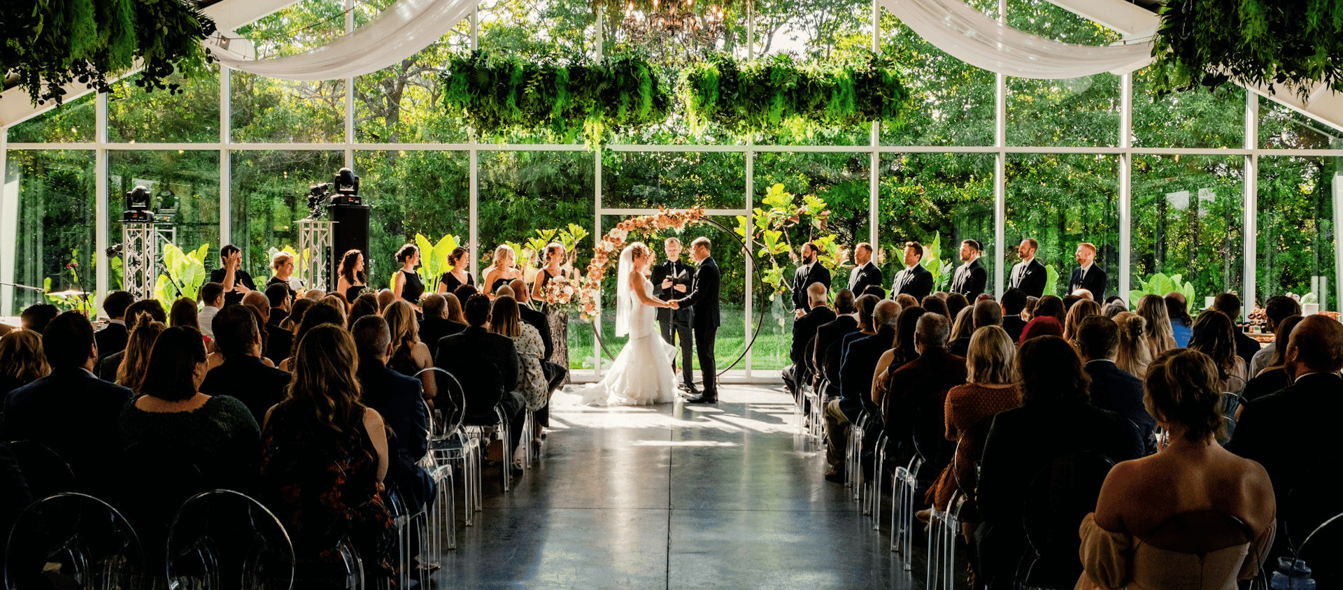 Bride and groom exchanging vows in a sunlit indoor venue with guests seated.