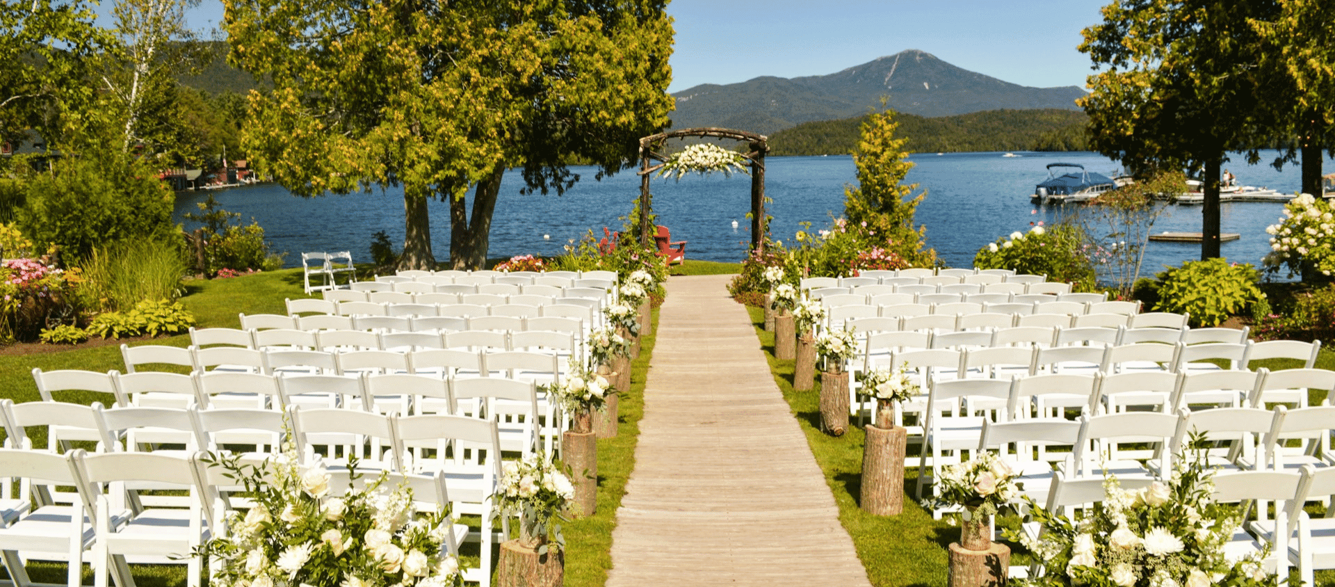 Outdoor wedding ceremony setup beside a lake with mountains in the background.