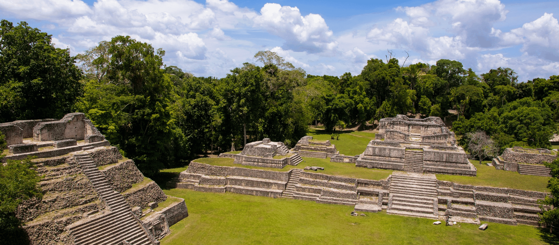 The Caracol Maya ruins rising above the rainforest canopy in the Cayo District of Belize under a blue sky.