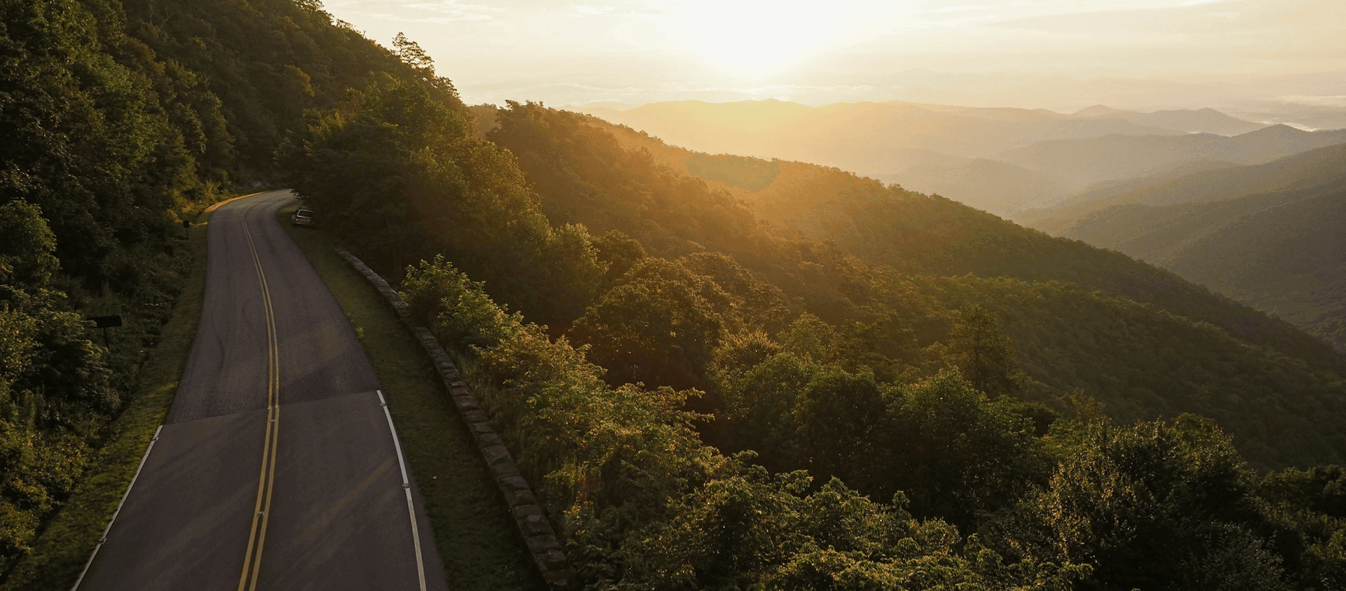 Winding road through forested mountains at sunset.