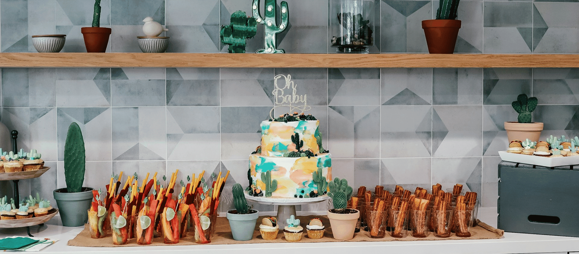 A decorated dessert table with a cake and cactus-themed treats for a baby shower.