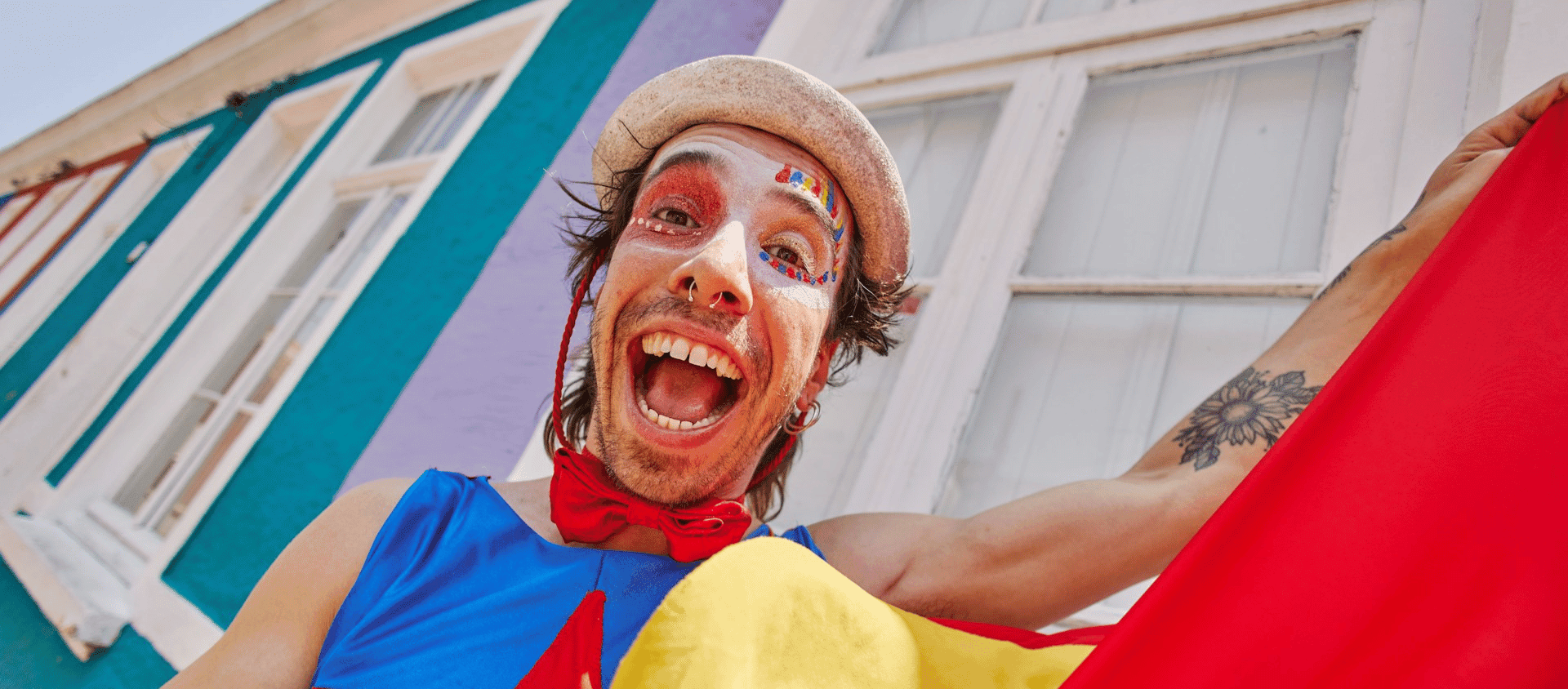 Festival performer wearing face paint and bright costume, smiling joyfully during a lively street celebration.