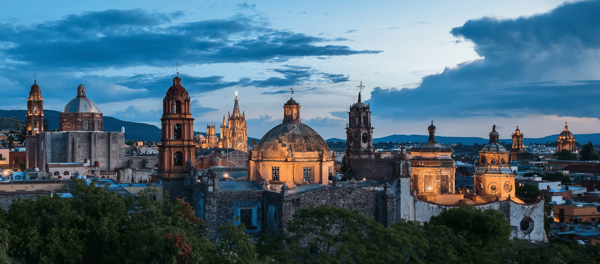 Historic city skyline with illuminated church domes and towers at dusk in central Mexico.