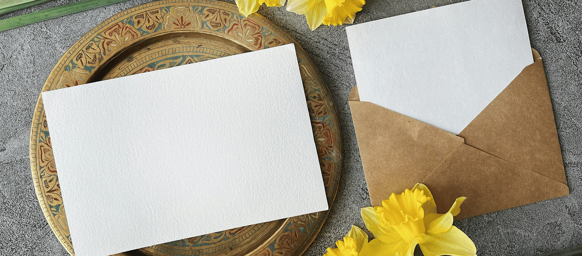 Minimal wedding invitation cards with kraft envelopes and yellow flowers on a decorative tray.