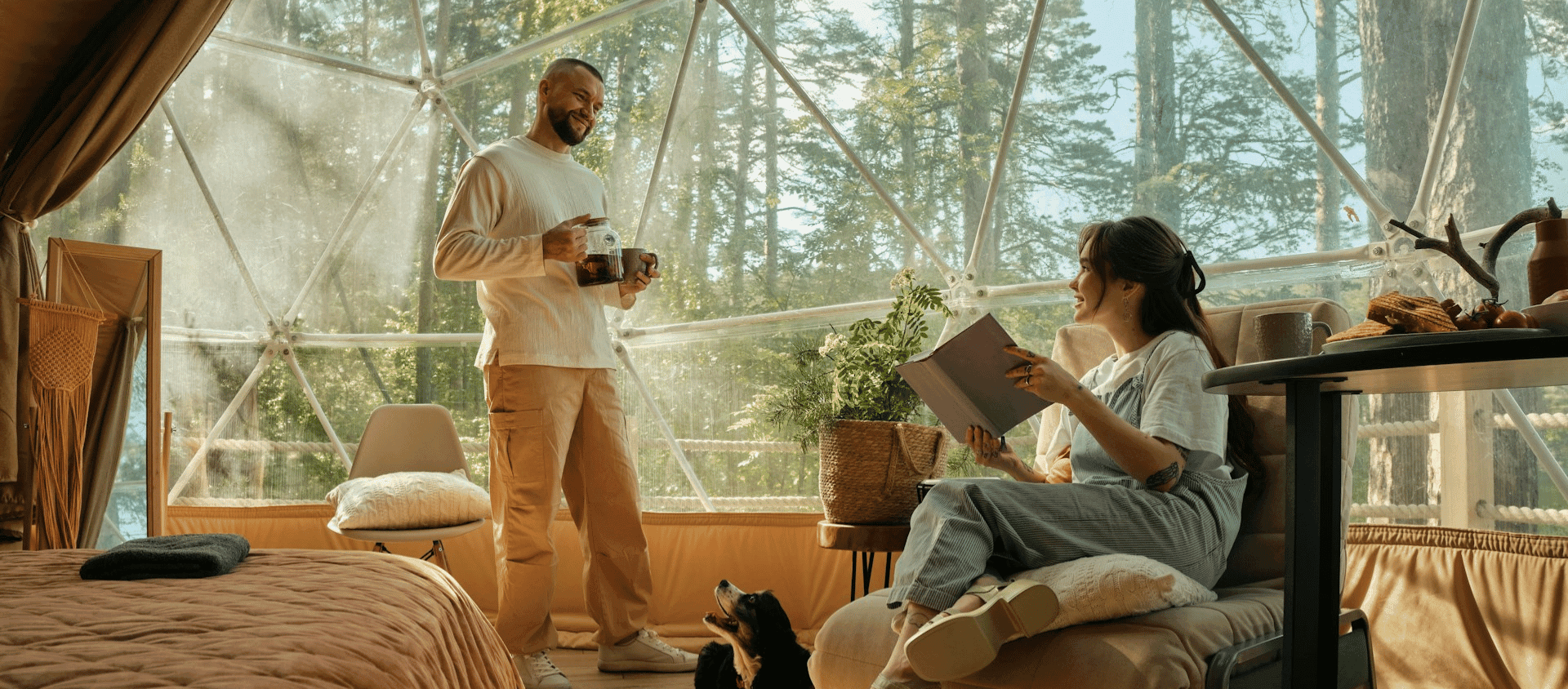 Couple relaxing inside a cozy geodesic glamping dome surrounded by forestry.