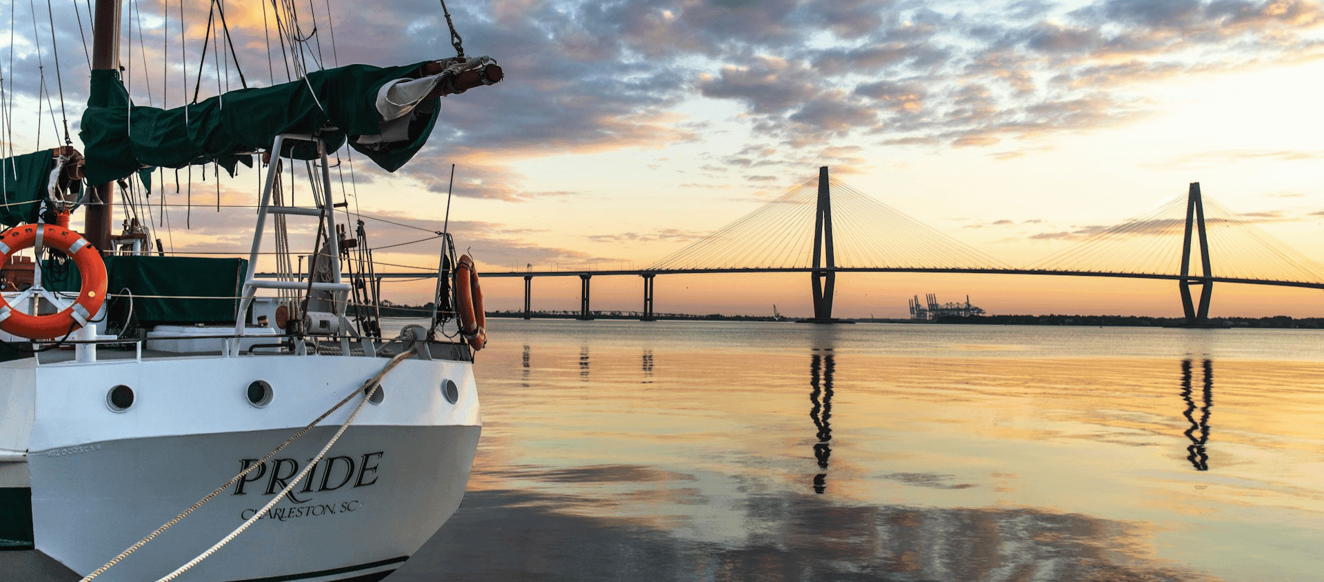 Sailboat at sunset on Charleston harbor with the Arthur Ravenel Jr. Bridge in the background.