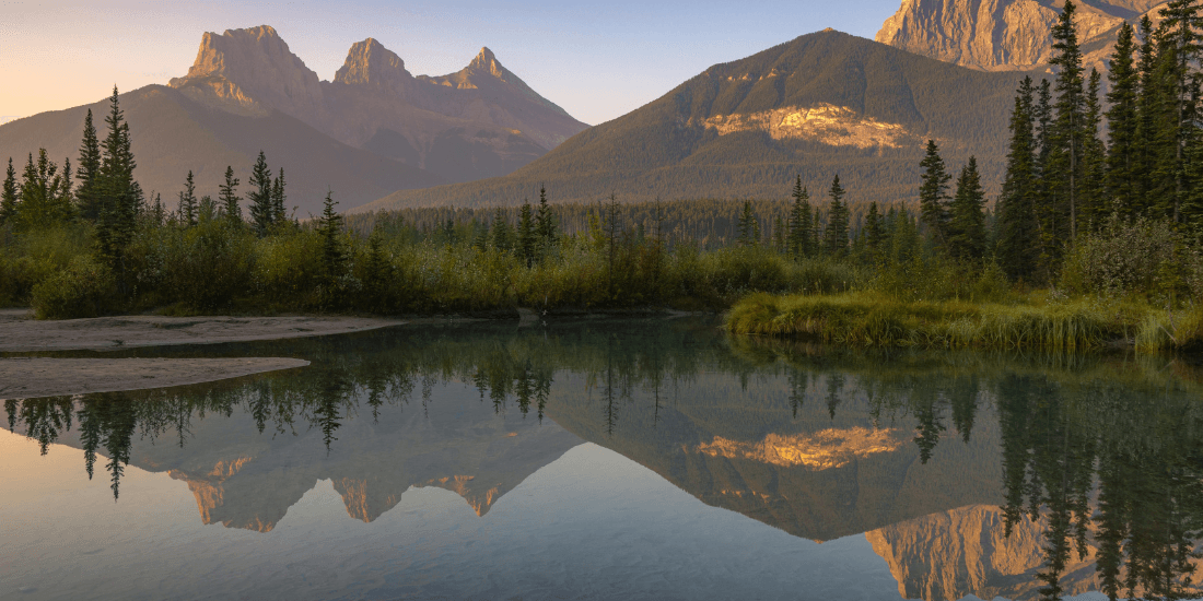 Mountain peaks reflected in a still lake surrounded by evergreen trees.