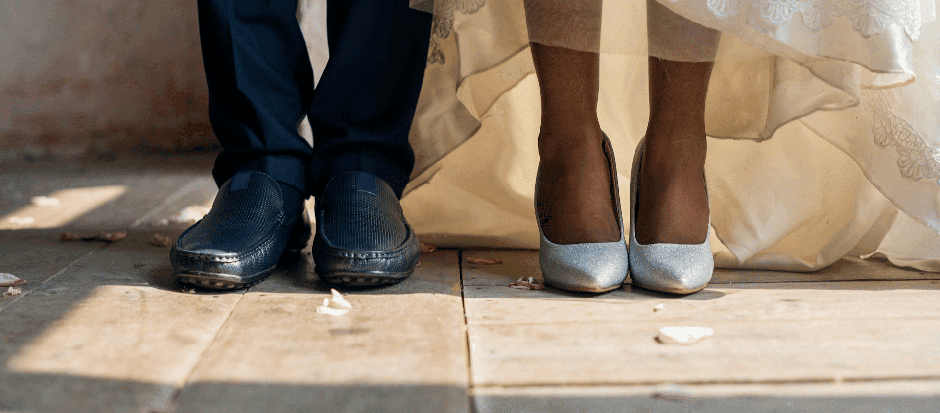 Close-up of the married couple's shoes on a wooden floor with scattered petals.