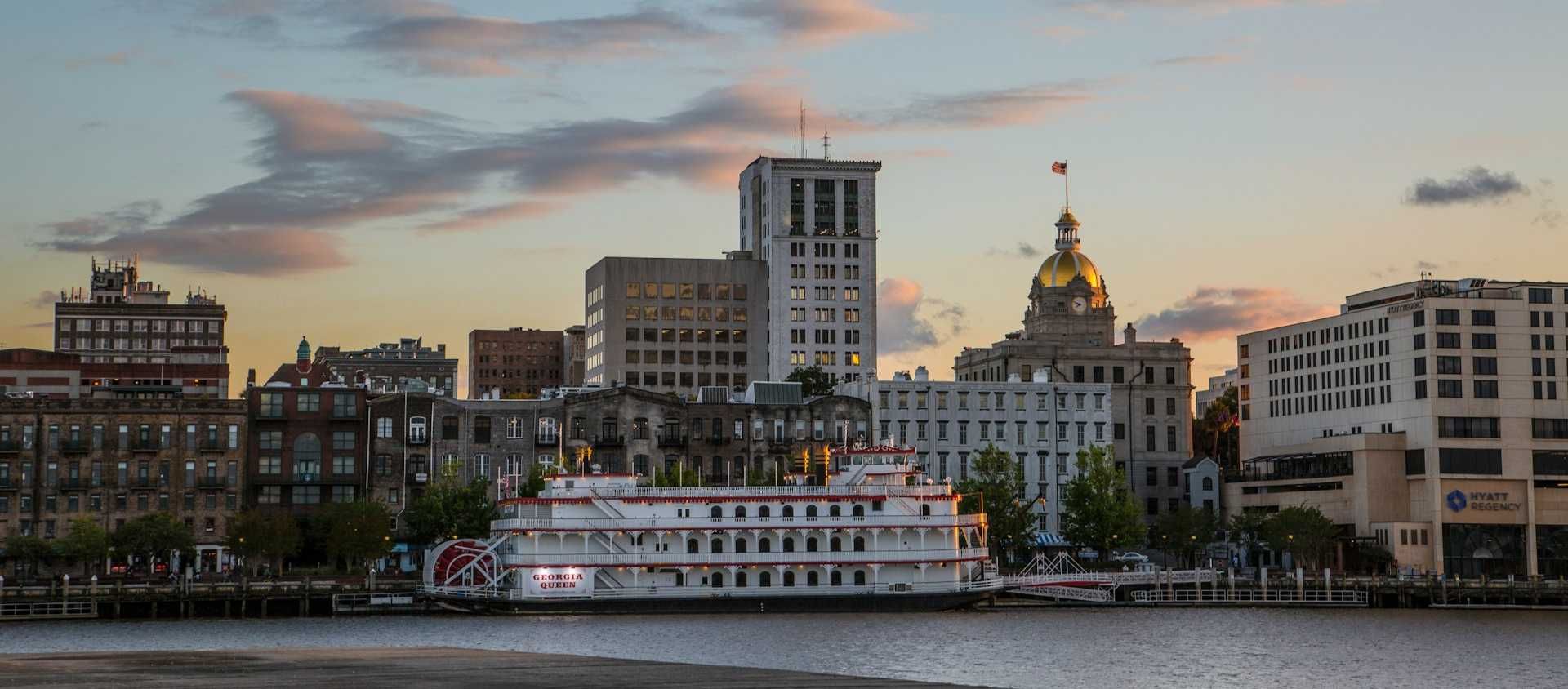 The Georgia Queen riverboat docked along the Savannah riverfront at sunset.