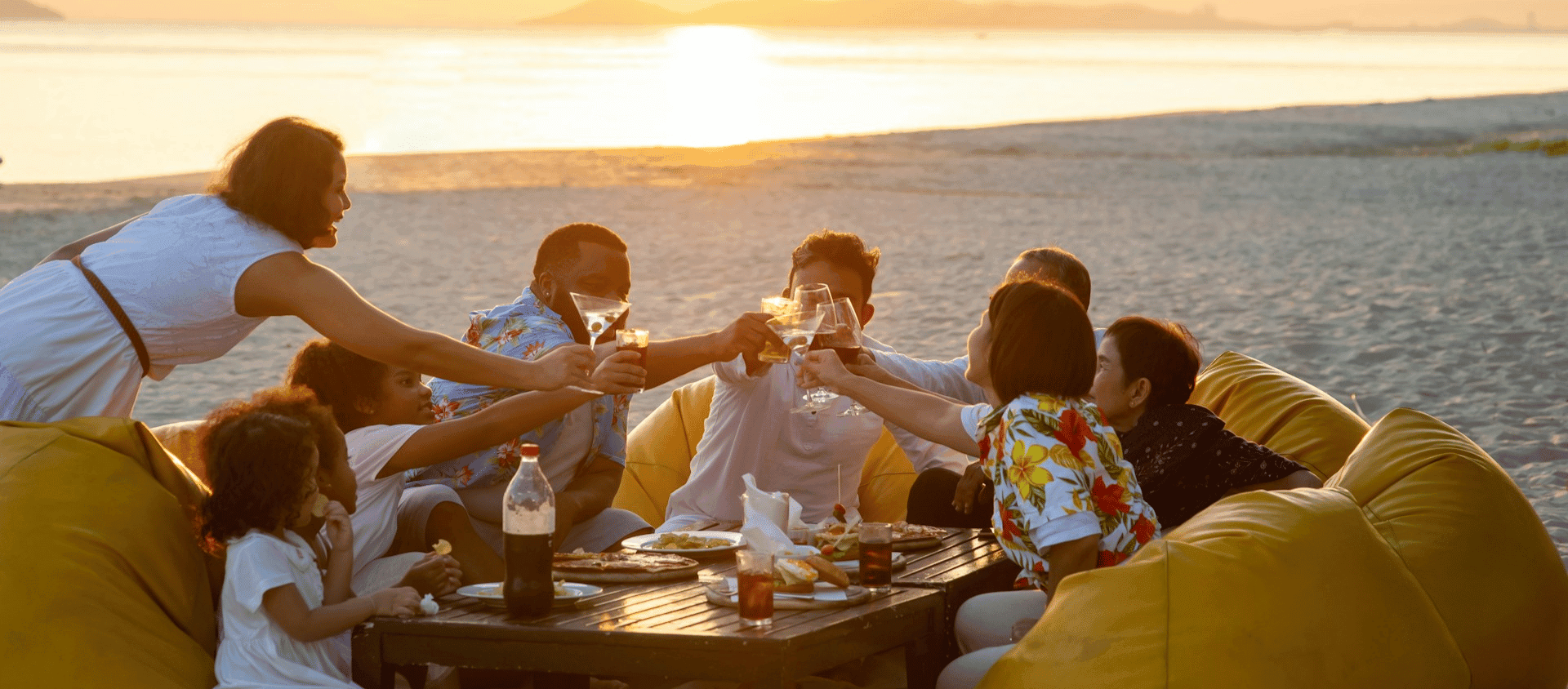 Group enjoying drinks together at a beach during sunset.