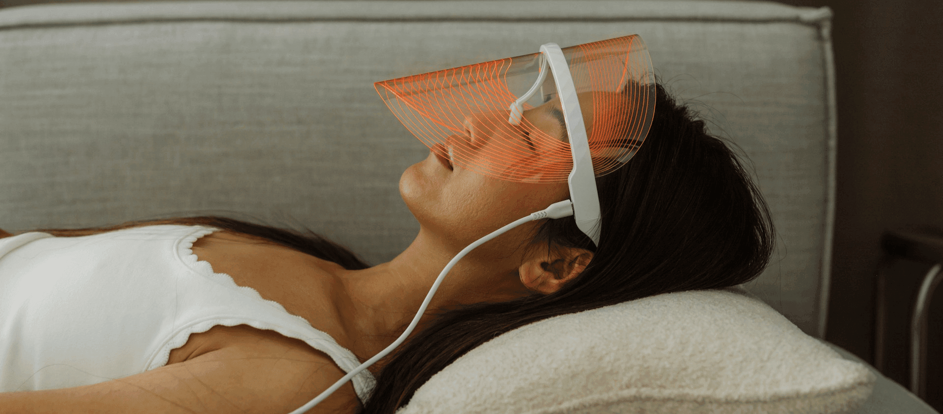 A woman lying down wearing a light therapy mask over her face.