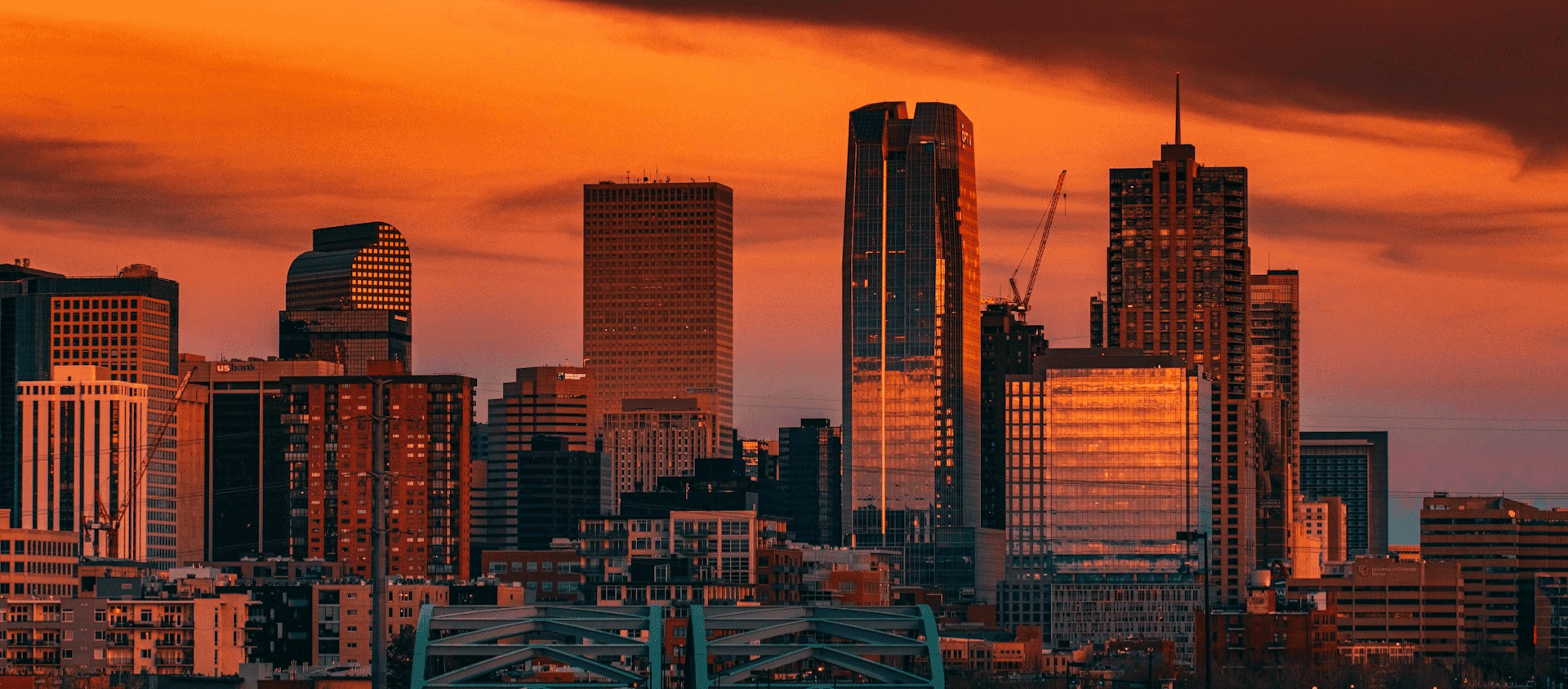 Downtown Denver skyline at sunset with glowing orange clouds above the city.