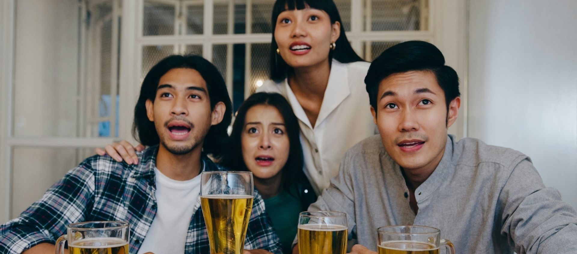Four friends watching an event together with glasses of beer on the table.