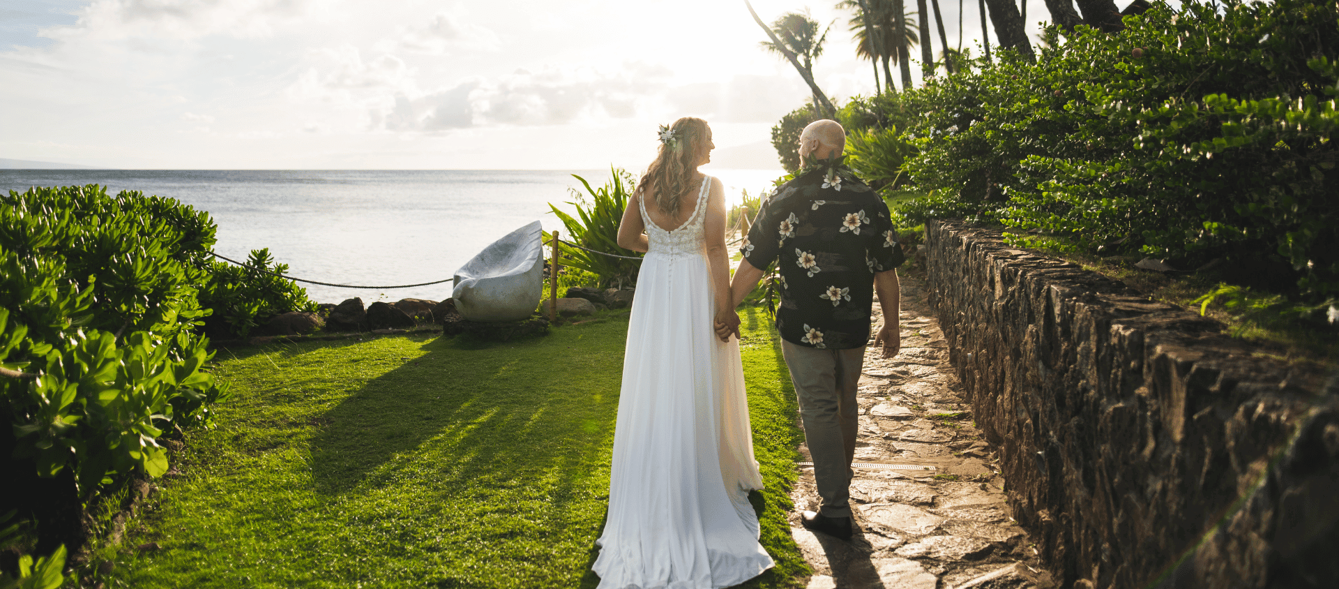 Couple walking along oceanfront path at Napili Kai Beach Resort at sunset.