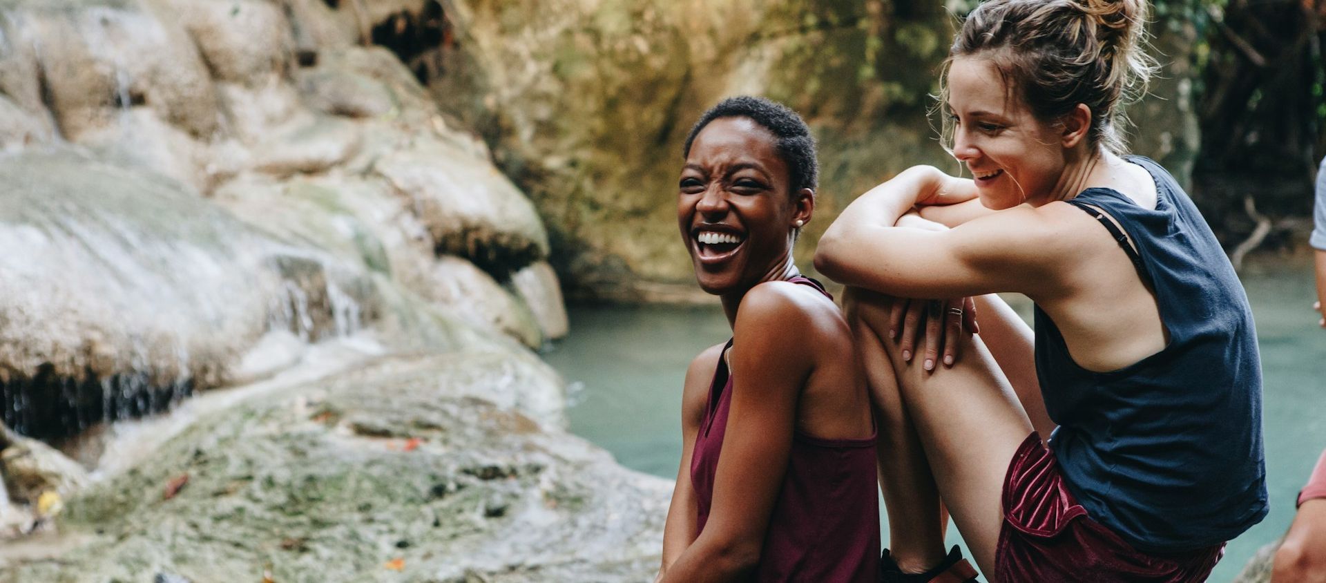 Two friends laughing outdoors near a waterfall.
