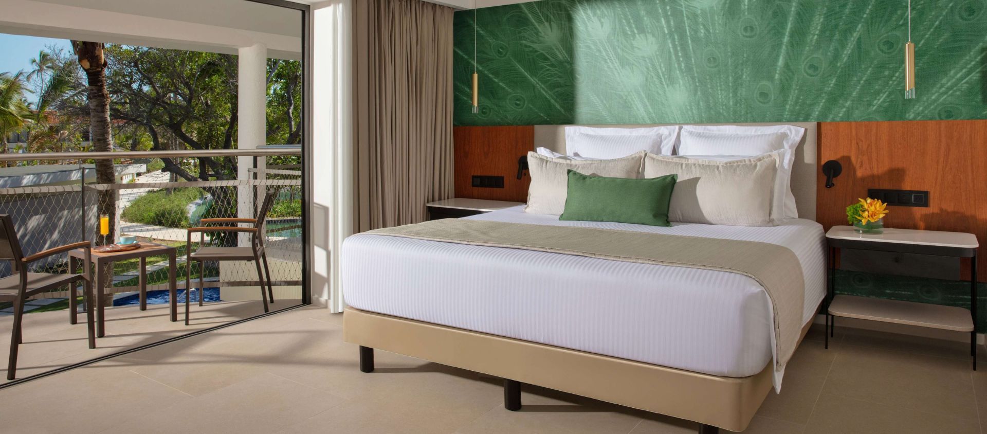 Resort guest room with a king bed, green accent wall, and a private balcony overlooking the pool.