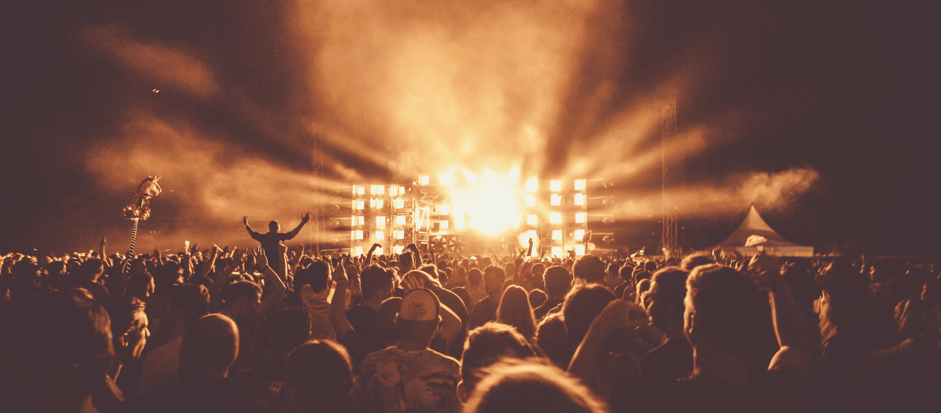 Crowd with hands raised at a concert lit by stage lights.