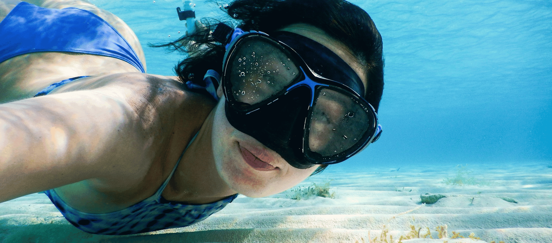 Person snorkeling underwater above a sandy ocean floor.