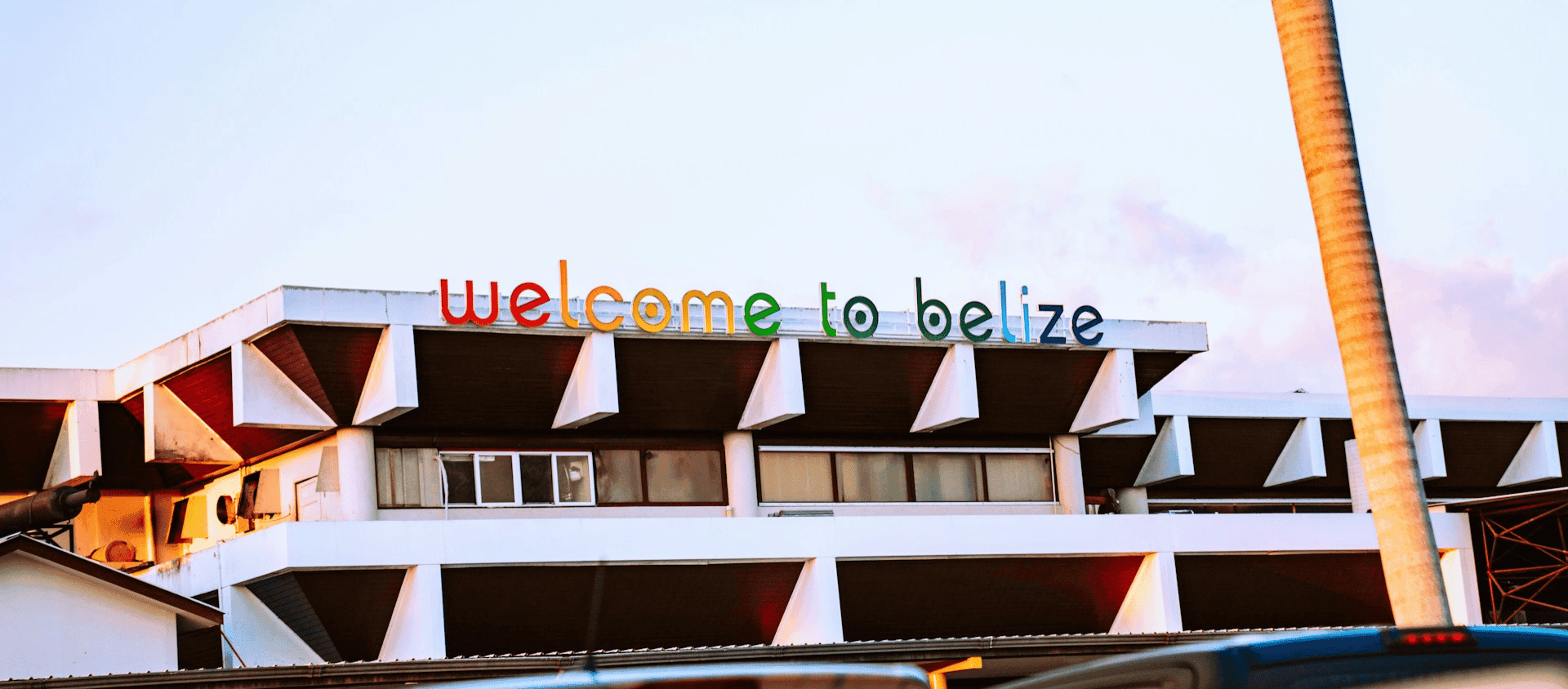 A colorful Welcome to Belize sign on a building at the Philip S.W. Goldson International Airport near Belize City at dusk.